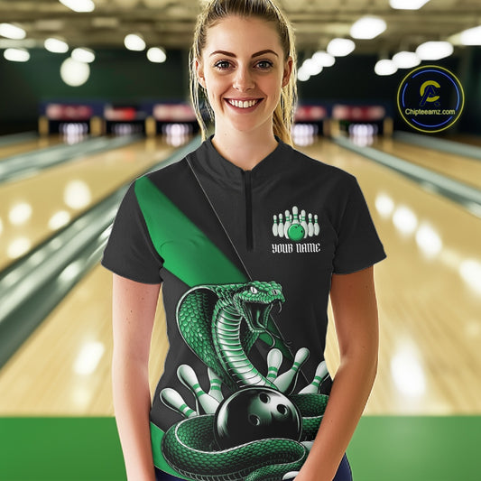 Female model in a bowling center wearing a black quarter-zip with green cobra artwork and bowling-themed accents.