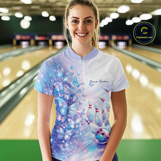 Female model wearing a bowling quarter zip with pastel purple and pink holographic butterflies and bowling artwork, front view at the bowling lane