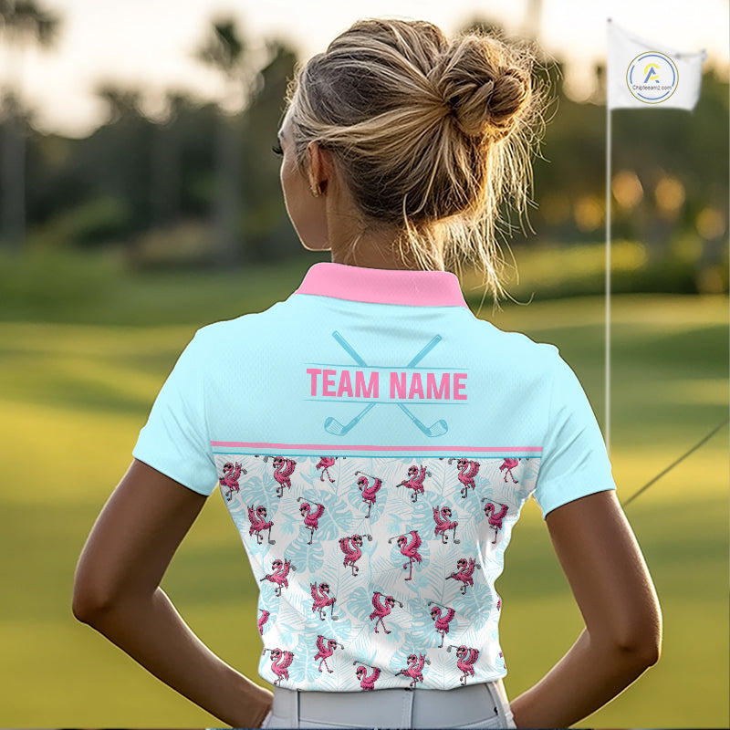 A woman on a golf course seen from behind, wearing a light blue short-sleeve polo shirt with a pink collar, pink 'TEAM NAME' text, and a pink flamingo pattern across the lower back.