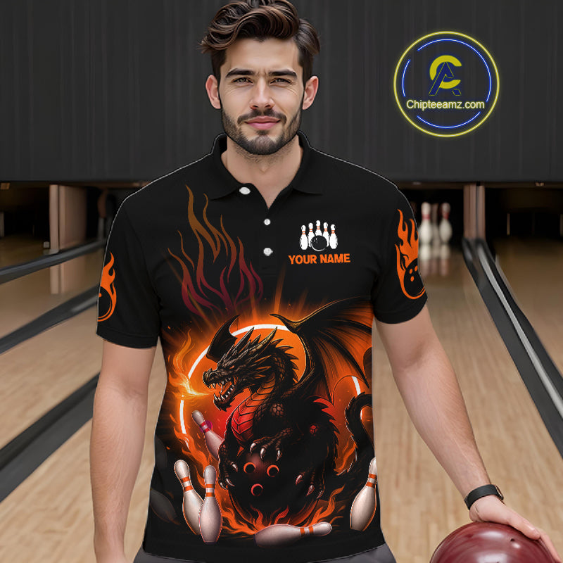 A man wearing a black short-sleeve polo shirt with a fiery dragon graphic and bowling pins, standing in a bowling alley. The shirt features orange flames, a black dragon, and bowling pins, with 'YOUR NAME' printed on the chest.