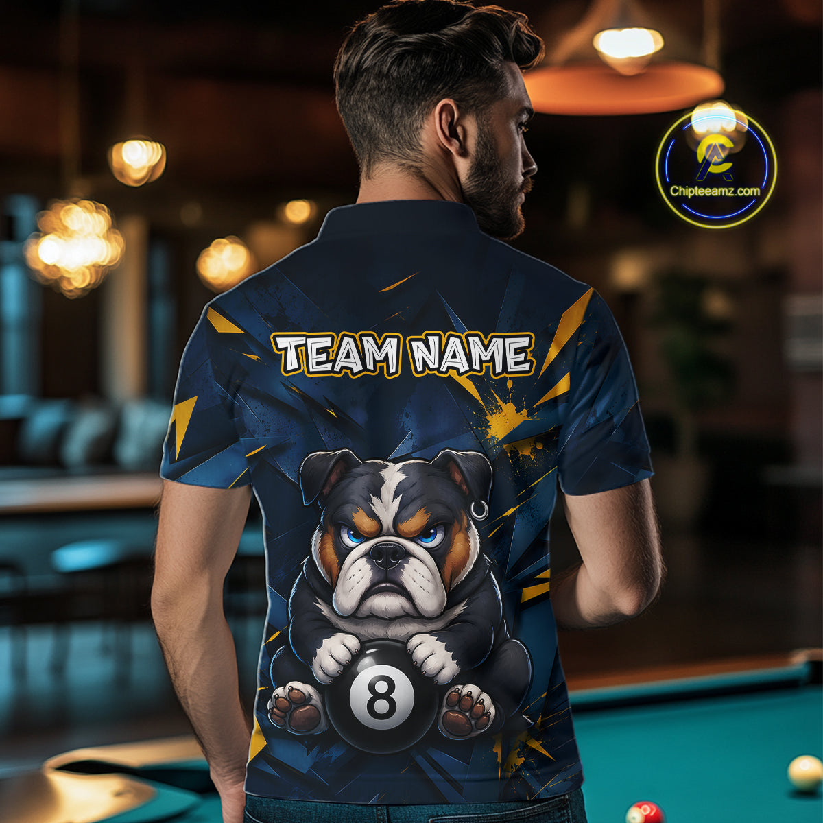 A back view of a custom black billiards polo shirt worn by a male model. The shirt features a funny bulldog on the back, with a large white 'TEAM NAME' text placeholder. The background is a billiards room with a table and hanging lights.