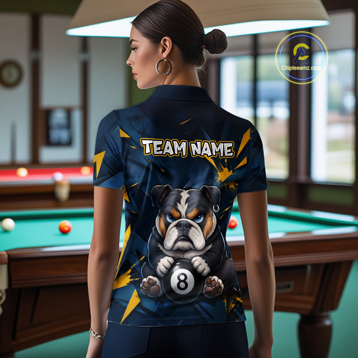 A back view of a custom black billiards polo shirt worn by a female model. The shirt features a bulldog on the back, with a large white 'TEAM NAME' text placeholder. The background is a billiards room with a table and hanging lights.