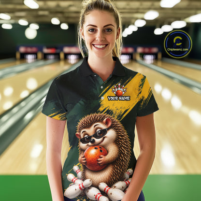 A woman stands in a bowling alley wearing a custom short-sleeve polo shirt with a hedgehog graphic holding a bowling ball and pins, with a yellow diagonal stripe and 'YOUR NAME' placeholder text on the chest. 