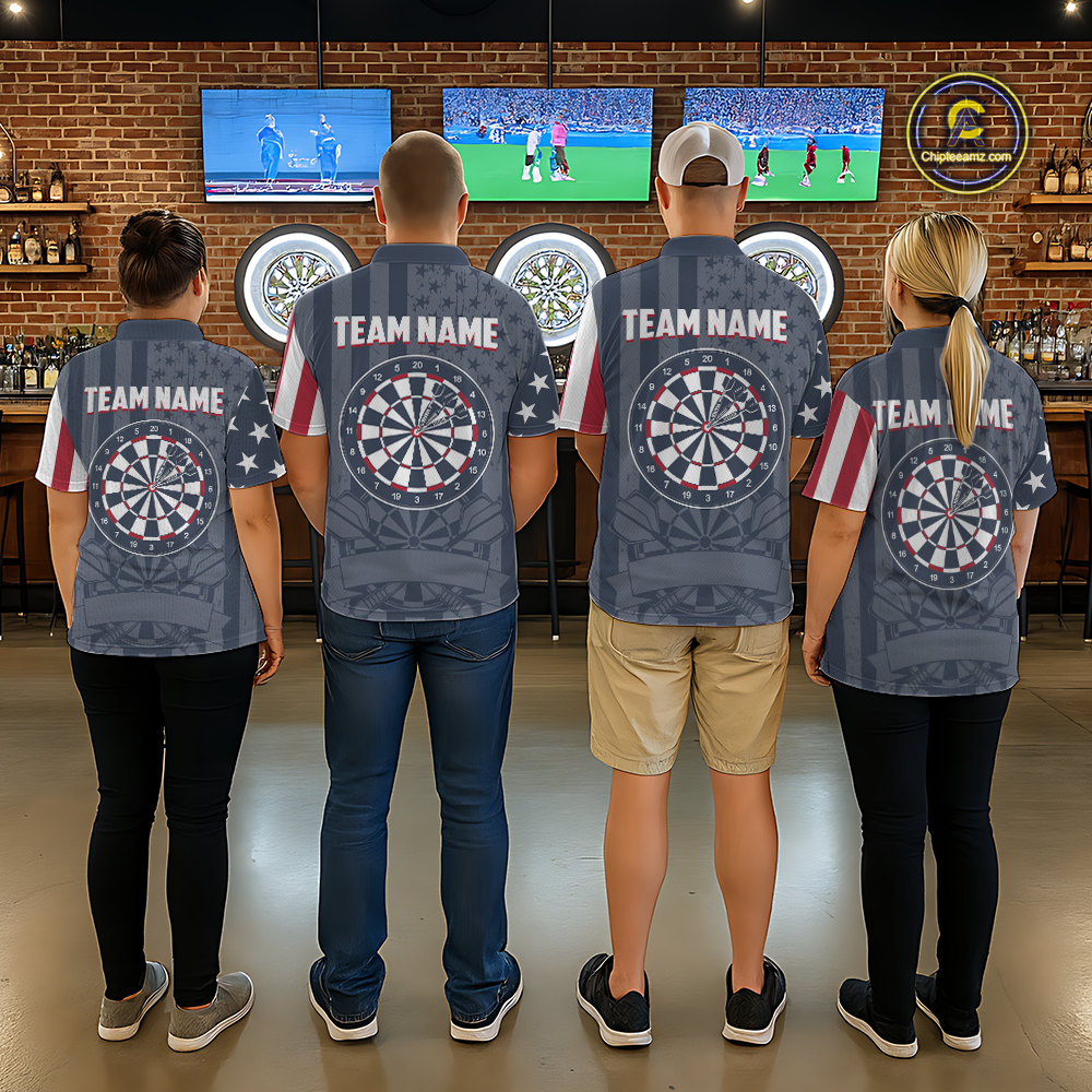 Darts team standing in front of electronic dartboards, showing the back of their matching uniform shirts with personalized team names and dartboard graphics.