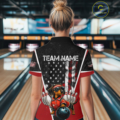 A woman viewed from behind wearing a custom bowling-themed short-sleeve collared shirt in a bowling alley. The shirt features a black and red American flag design with white stars, a cartoon dachshund bowling dog graphic, and the text 'TEAM NAME'.