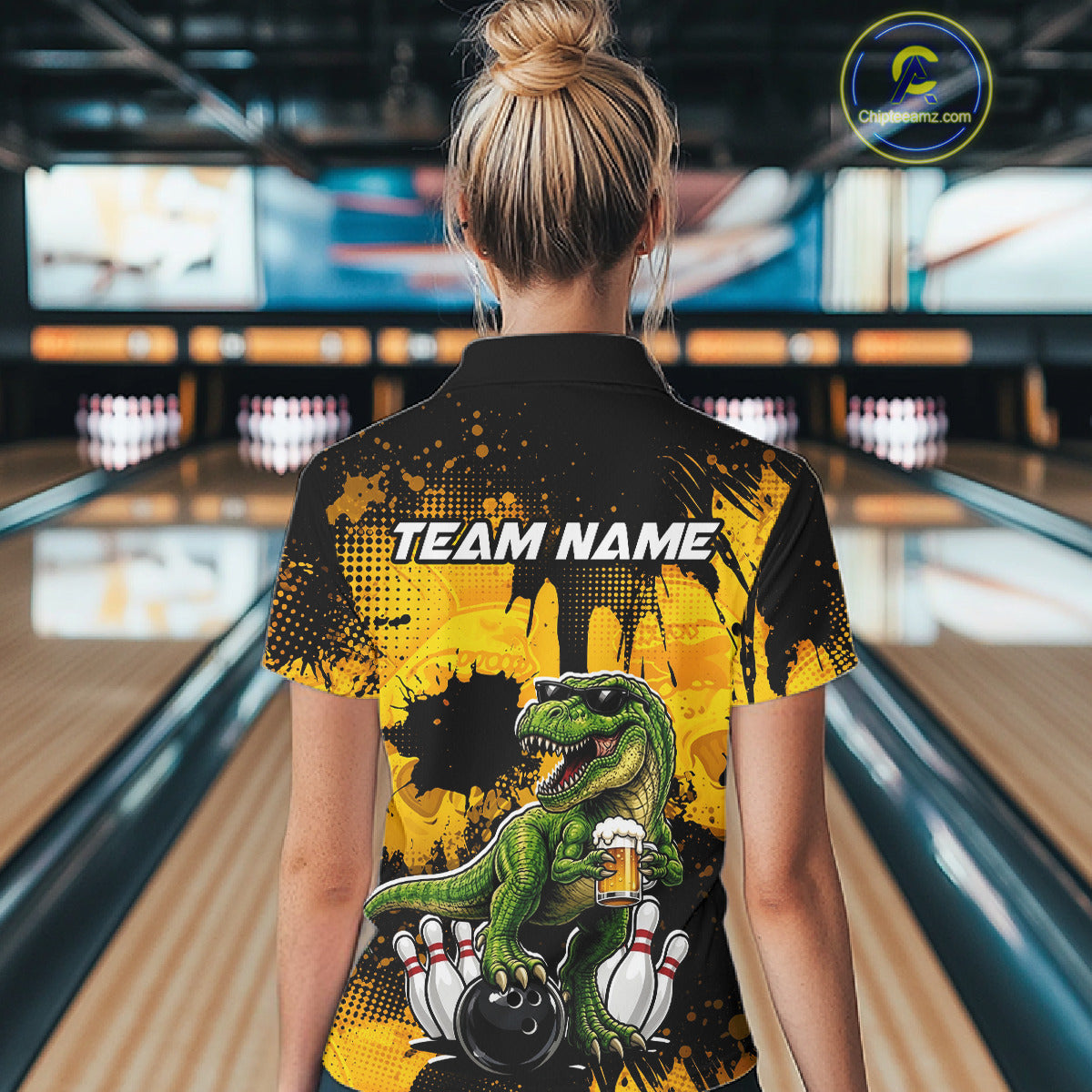 Women wearing bowling polo shirt featuring a dinosaur holding beer with bowling pins and ball artwork on black yellow background.