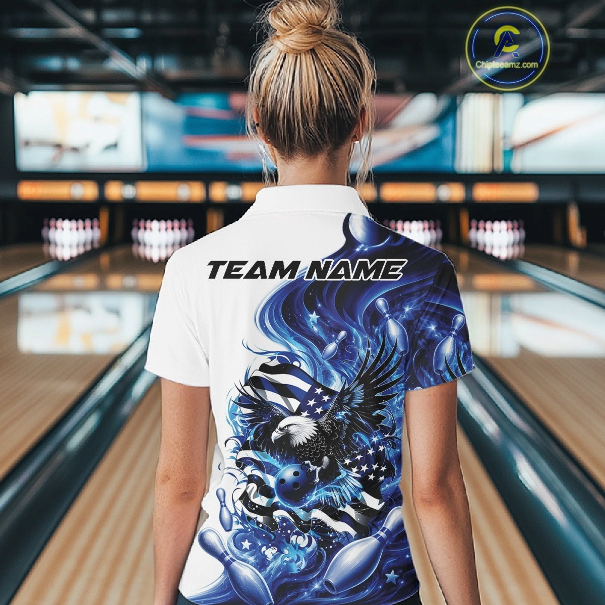Back view female model in a bowling lane wearing a white and blue quarter zip shirt with eagle artwork and flowing American flag inspired accents.