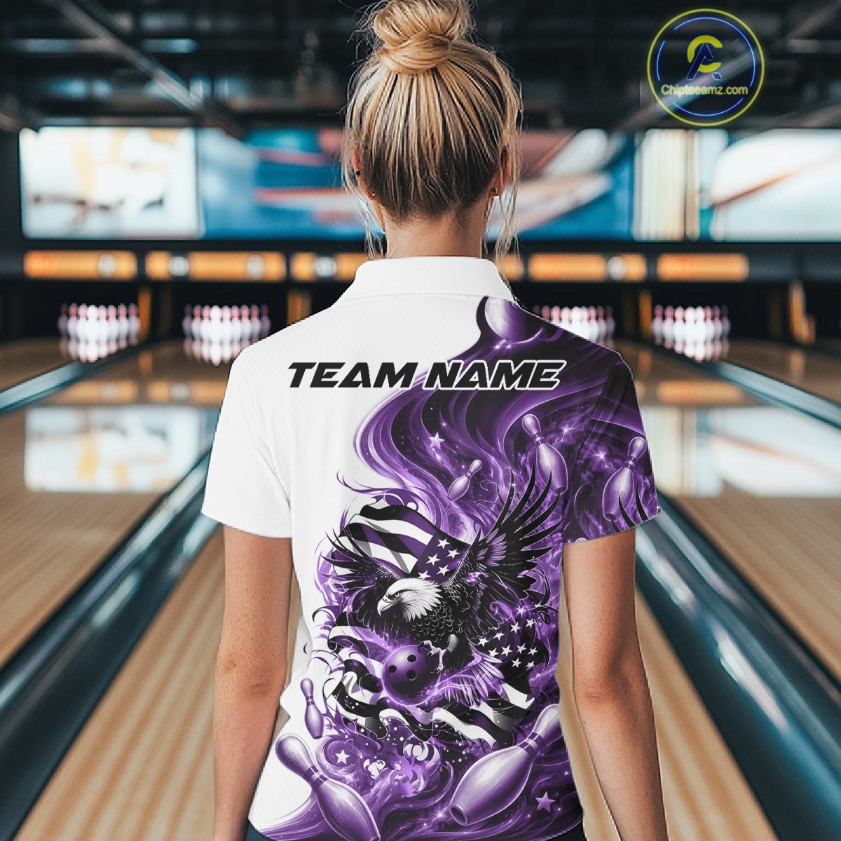 Female model back view at the bowling lane wearing a white and purple quarter zip shirt with eagle artwork and flowing flag inspired accents.