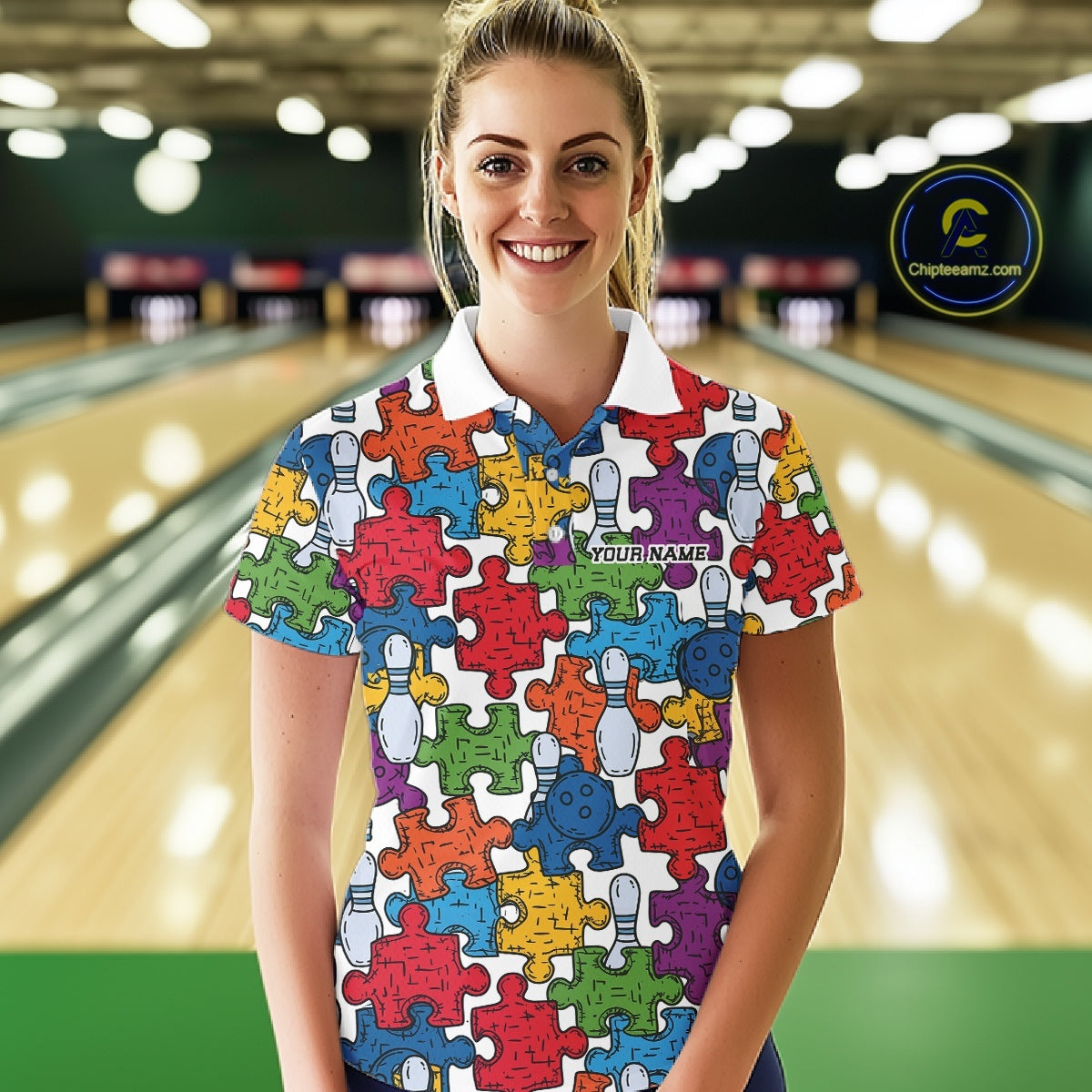 A woman standing in a bowling alley wearing a short-sleeve polo shirt covered in a colorful jigsaw puzzle pattern with bowling pins and smiley faces. 