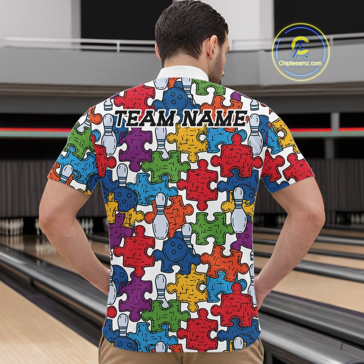 A man viewed from behind wearing a short-sleeve collared shirt with a colorful bowling-themed puzzle pattern. The shirt features multicolored puzzle pieces in red, blue, green, yellow, purple, and orange, interspersed with white bowling pins and bowling balls.