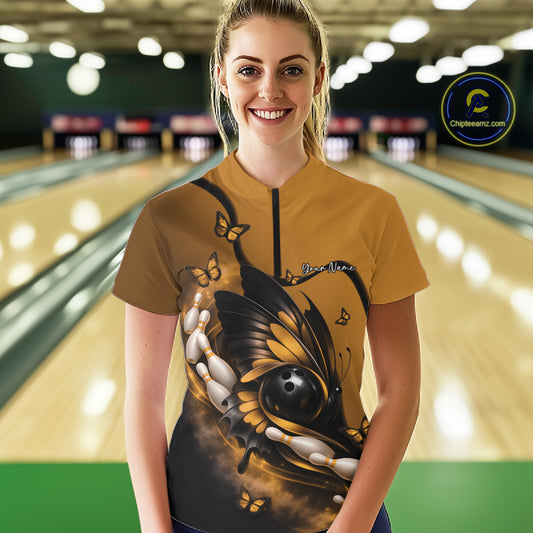 Female model shown from the front in a bowling center wearing a yellow and black quarter-zip shirt with butterfly, bowling ball, and pin graphics.