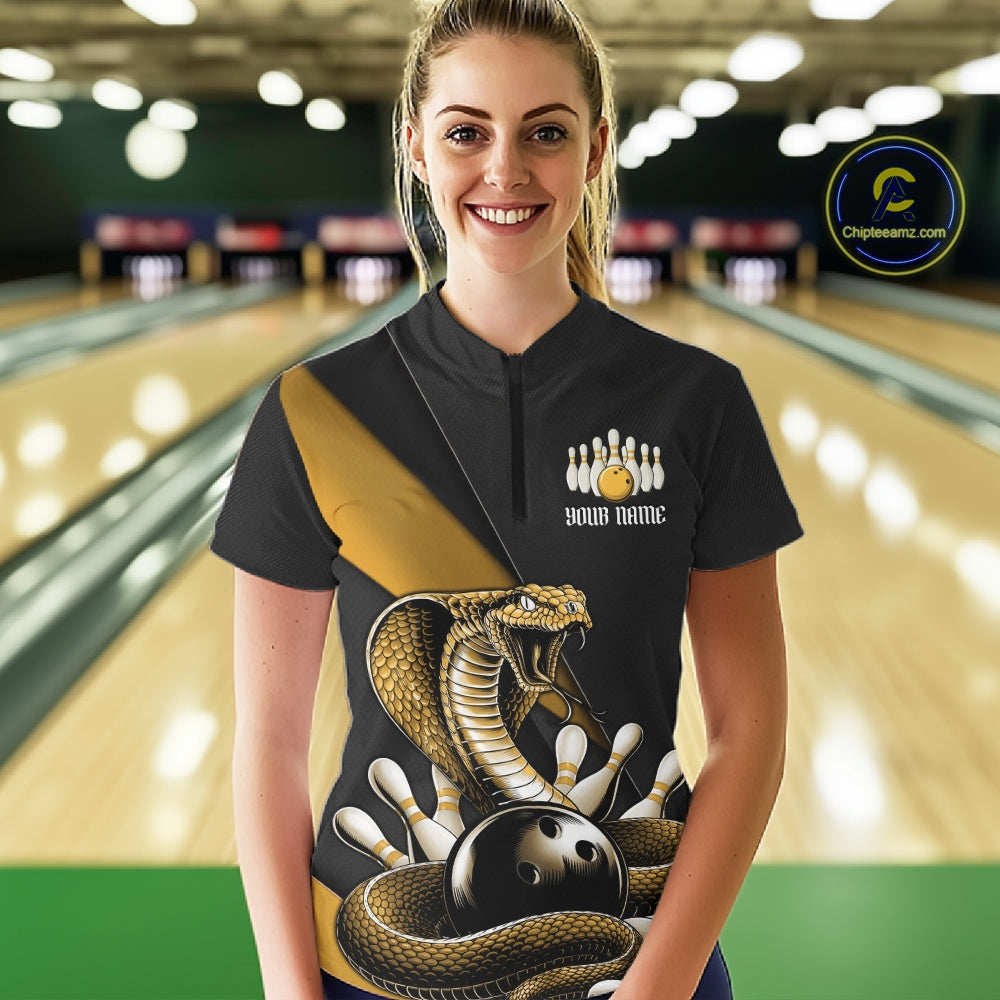 Female model in a bowling lane wearing a black quarter-zip decorated with yellow cobra artwork and bowling pin graphics.
