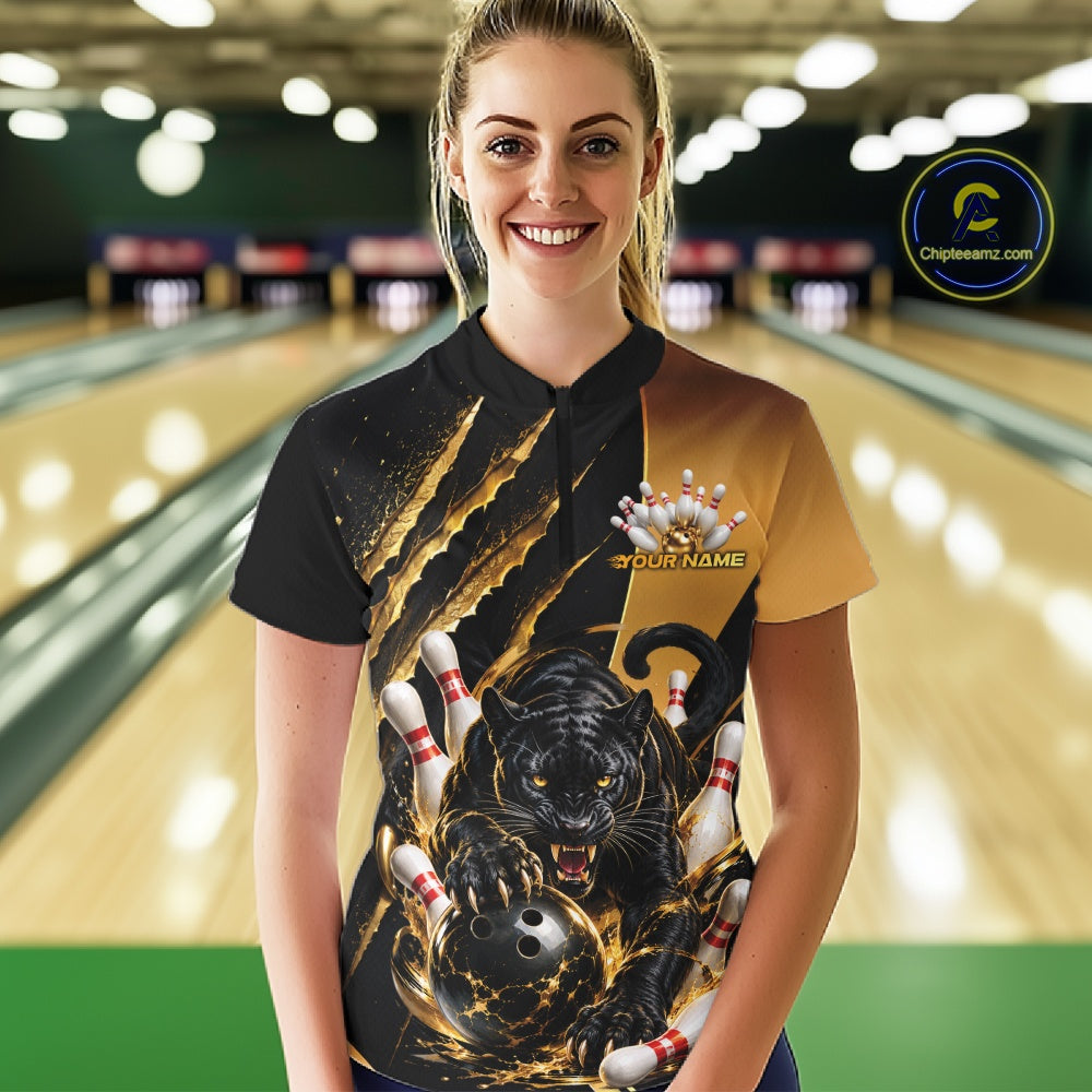 A woman stands in a bowling alley wearing a custom bowling shirt with a black and gold design featuring a black panther, bowling balls, and pins. The shirt has a split black and gold color scheme with a graphic print on the front.