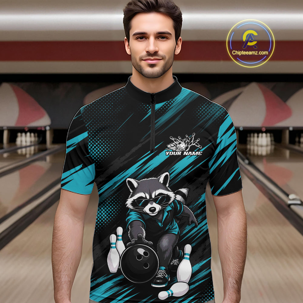 A man wearing a short-sleeve bowling-themed quarter-zip shirt with a raccoon graphic and teal diagonal stripes, standing in a bowling alley. The shirt has a black base with bright teal accents and a raccoon holding bowling pins and a bowling ball, with 'YOUR NAME' printed on the chest.