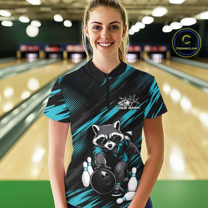 A woman stands in a bowling alley wearing a custom short-sleeve bowling shirt. The shirt features a black and teal graphic design with a raccoon holding a bowling ball and pins, and a white placeholder logo that reads 'YOUR NAME'.