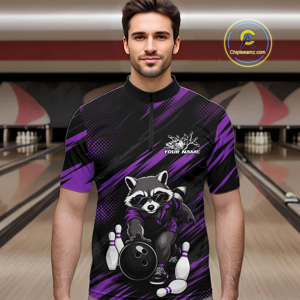A man wearing a short-sleeve black and purple bowling-themed quarter-zip shirt with a raccoon graphic, standing in a bowling alley. The shirt features a raccoon holding a bowling ball and pins, with 'YOUR NAME' printed on the chest.