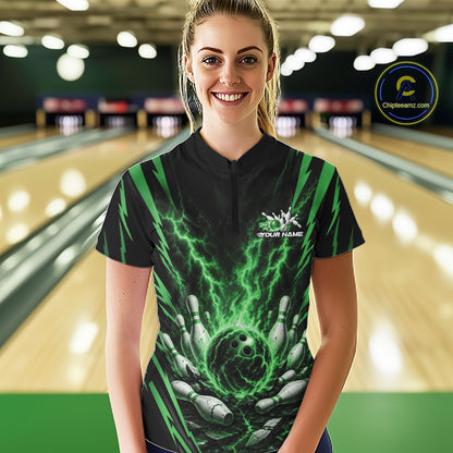 A woman stands in a bowling alley wearing a black short-sleeve bowling quarter zip jersey with a green lightning and bowling pins graphic. 