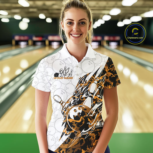 Female model wearing a white bowling polo shirt at the lane with orange camo bowling artwork and subtle ball patterns.