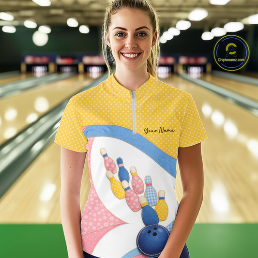 Female model at a bowling lane wearing a quarter-zip bowling shirt with vibrant patchwork bowling ball and pin artwork accented by polka dots.