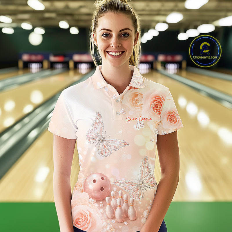 Female model in a bowling alley wearing a bowling polo shirt with pastel glitter butterfly artwork floating above bowling pins and a bowling ball.