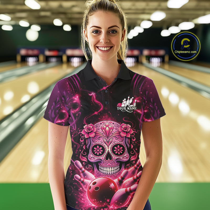 Female model at a bowling lane wearing a black and pink polo shirt with sugar skull artwork and vibrant bowling-themed design.