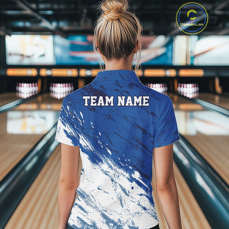 Back view of a female bowler wearing a white and blue bowling quarter-zip shirt with a splatter-inspired sports jersey design in a bowling lane
