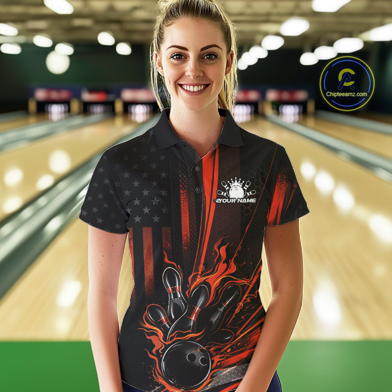 Female model at a bowling lane wearing a black and orange polo shirt with patriotic bowling ball striking pins and flag-inspired graphics.