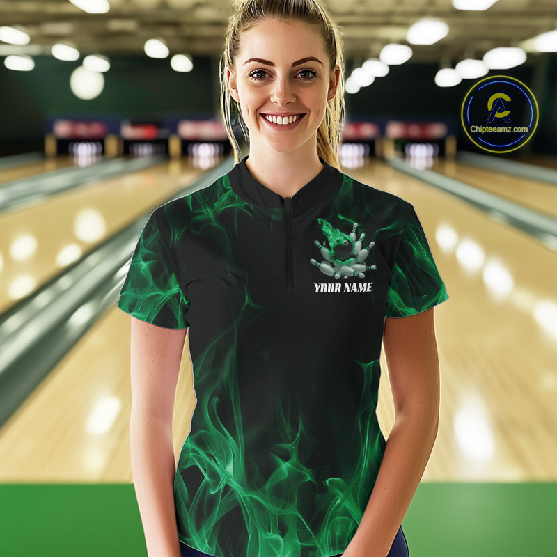 Female model at a bowling lane wearing a black and green bowling quarter-zip shirt with bowling strike artwork, scattered pins, and flame effects.