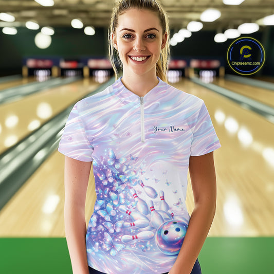 Female model wearing a bowling quarter zip with pastel purple and pink holographic butterfly graphics and bowling accents, front view at the bowling lane