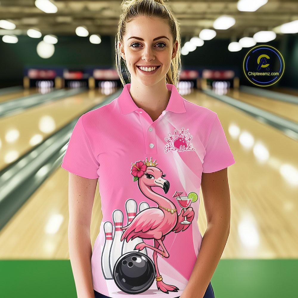 Female model wearing a pink bowling polo shirt at a bowling lane with a crowned flamingo, cocktail, bowling ball, and hibiscus flower artwork.