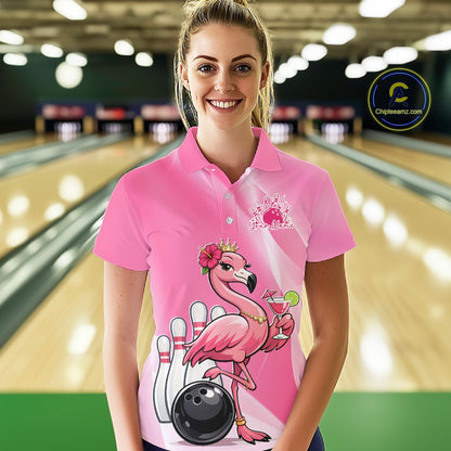 Female model wearing a pink bowling polo shirt at a bowling lane with a crowned flamingo, cocktail, bowling ball, and hibiscus flower artwork.