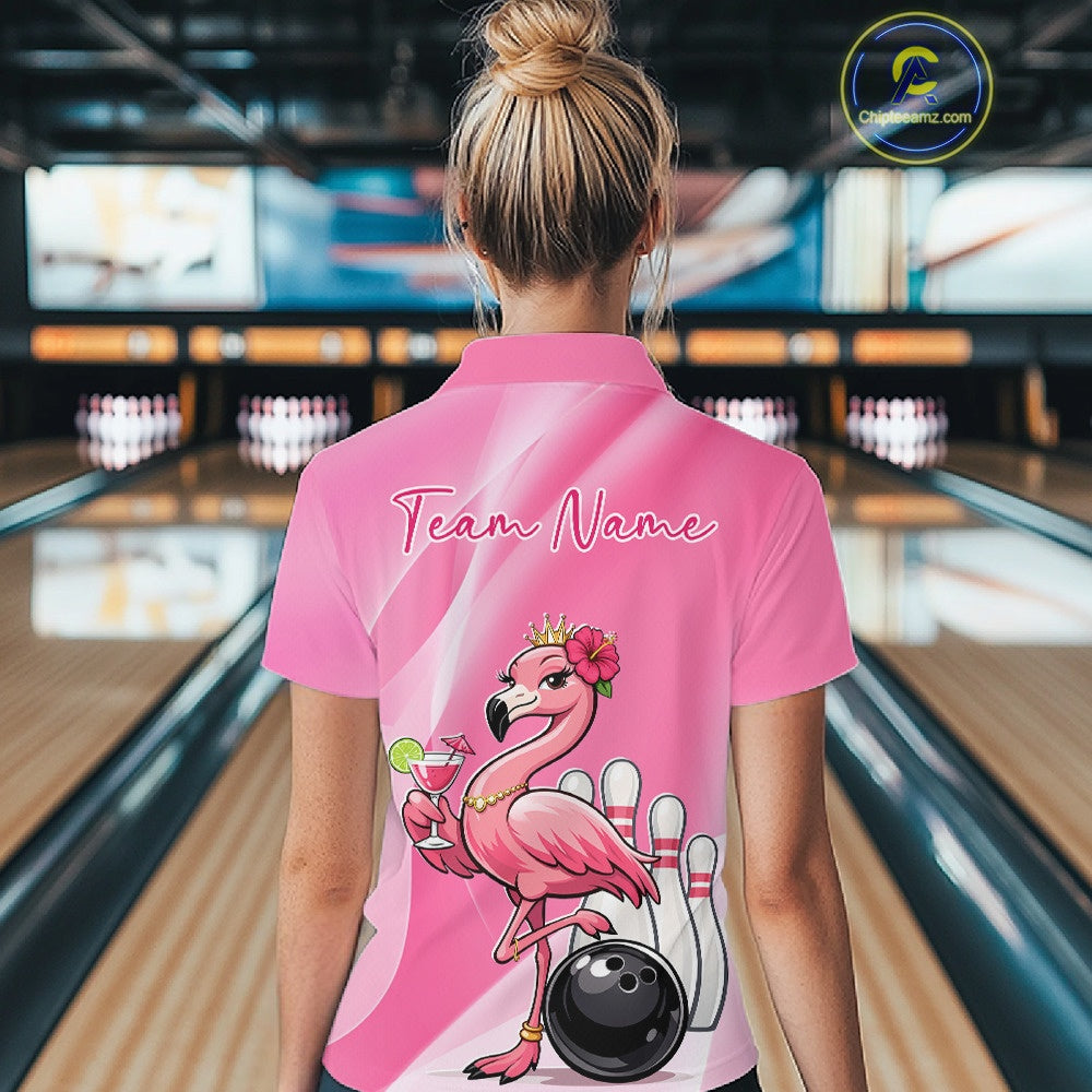 Back view of a female model in a bowling venue wearing a pink polo shirt featuring a crowned flamingo beside a bowling ball with hibiscus flowers.