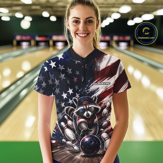 Front view of a female model wearing a bowling quarter zip shirt featuring a raccoon in patriotic sunglasses rolling a bowling ball through scattered pins with a distressed American flag backdrop in a bowling lane.