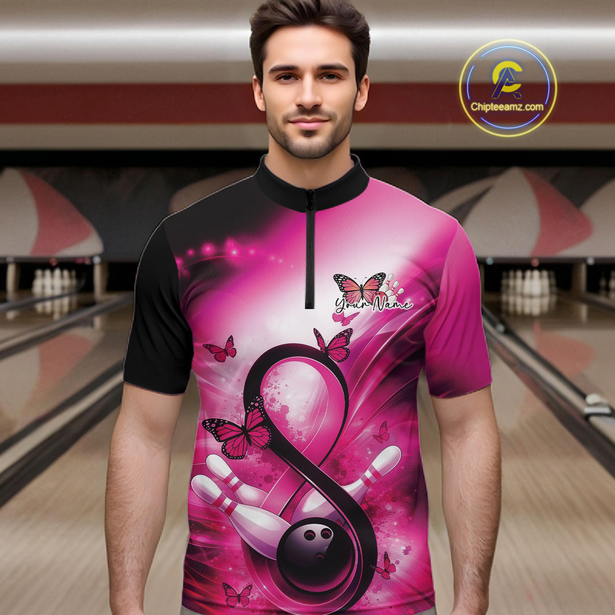 Male model in a bowling alley wearing a quarter-zip shirt with a pink ribbon, bowling ball, and butterfly illustration.