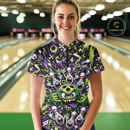 Front view of a female model at a bowling lane wearing a green and purple bowling quarter-zip shirt featuring a mischievous green monster bowling ball with sharp teeth, a purple tongue, playful hand gesture, and cheerful cartoon bowling pins.