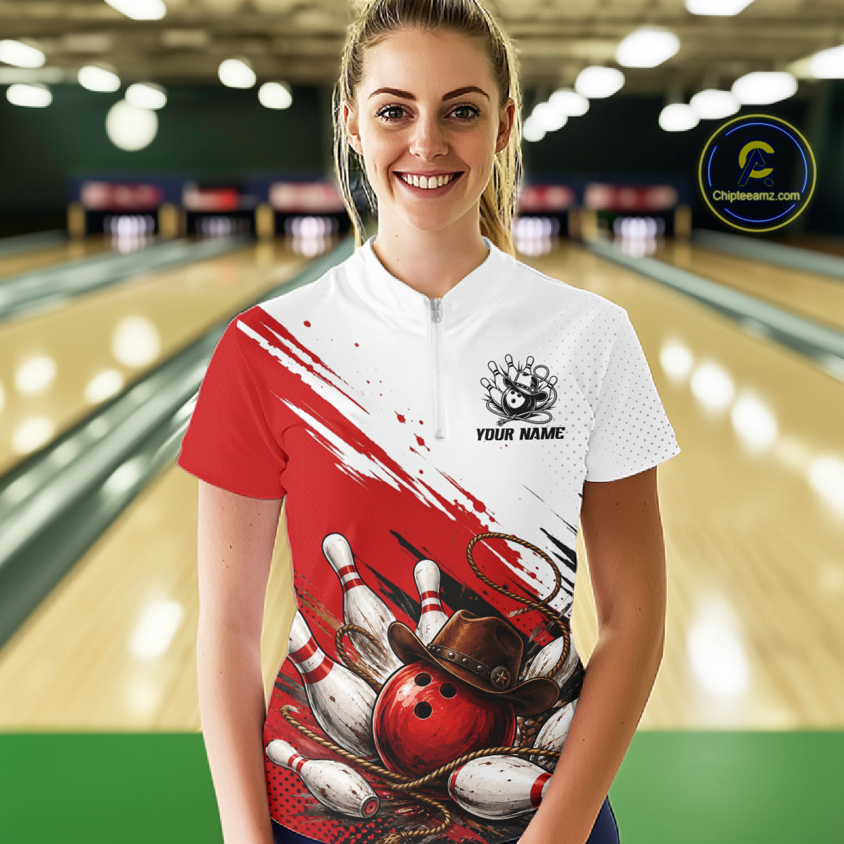 A woman stands in a bowling alley wearing a short-sleeve bowling shirt with a red and white design featuring bowling pins, balls, and a cowboy hat graphic. The right side of the shirt is solid red, while the left side is white with a zipper and a bowling pin graphic.