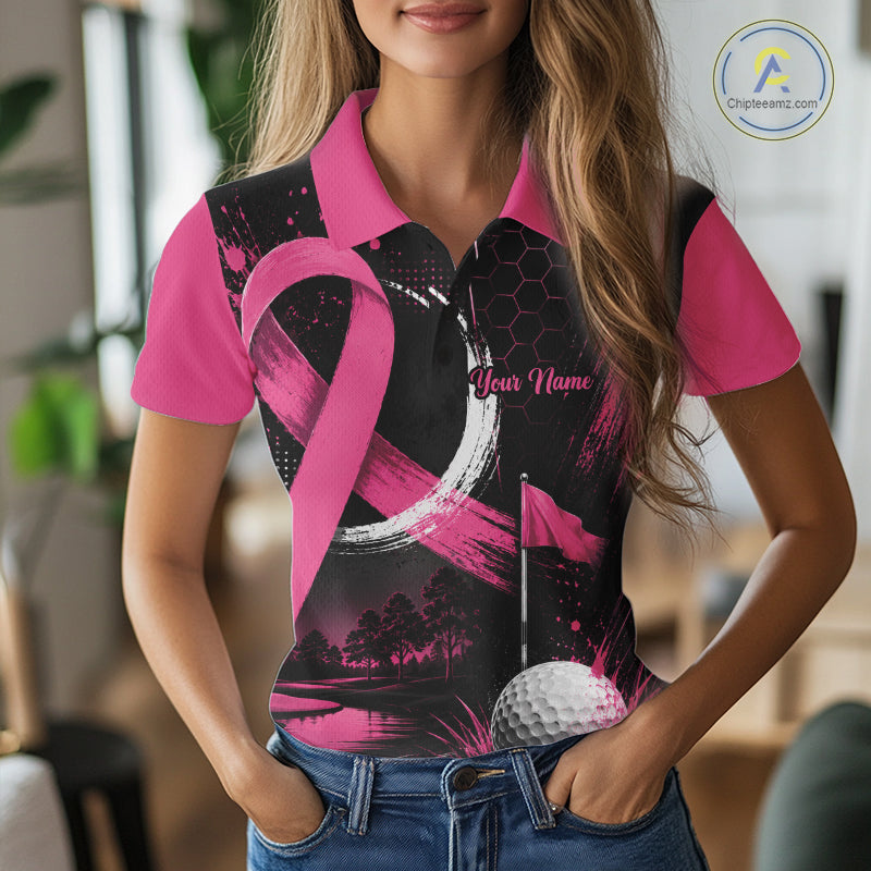A woman wearing a short-sleeve polo shirt with a pink and black graphic design featuring a ribbon motif, golf flag, and golf ball, paired with blue jeans in a blurred indoor setting.