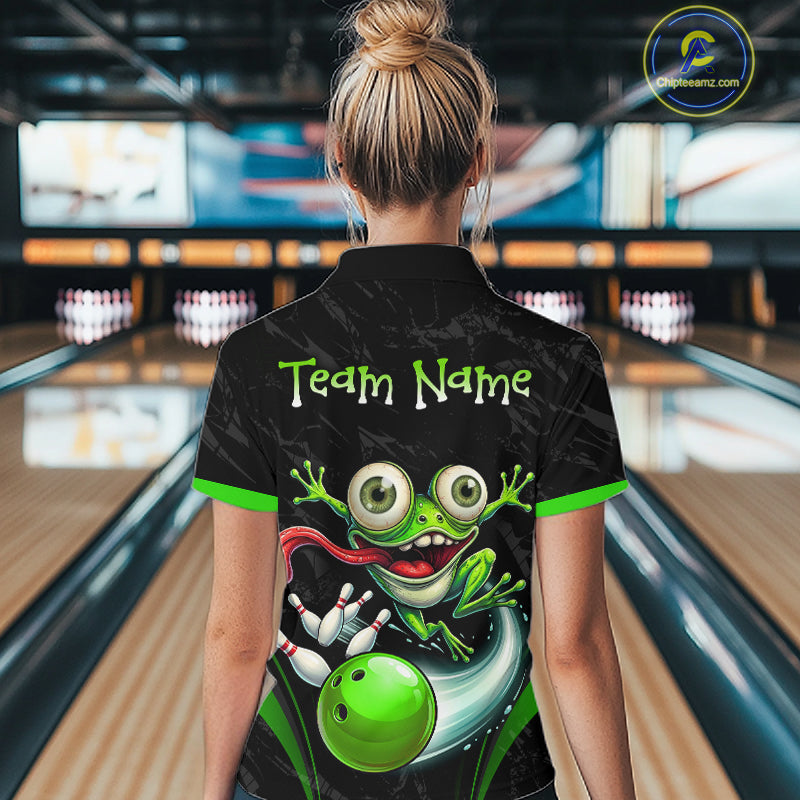 A woman viewed from behind wearing a black bowling-themed short-sleeve polo shirt with a cartoon green frog graphic and the text 'Team Name' on the back. The background shows blurred bowling alley lanes and pins.