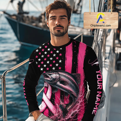 A man wearing a long-sleeve custom crewneck shirt with a pink and black American flag design, a large fish graphic, and 'YOUR NAME' printed on the sleeve, standing on a boat with water and another boat in the background.
